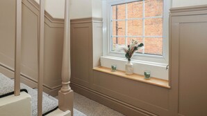A staircase with a white balustrade, a window with a brick wall view, and a shelf with a vase and candles. - Broadwath Old House (Brampton)