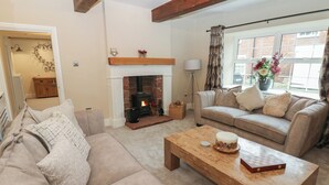 A cozy living room with a fireplace, a sofa, a coffee table, and a window with curtains. - Broadwath Old House (Brampton)