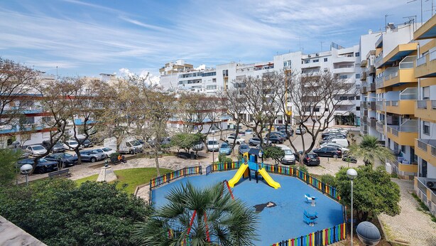 Un quartier résidentiel avec une aire de jeux, des voitures garées et des immeubles d’habitation.
