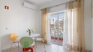 Une pièce comprenant une table à manger, des chaises, une plante en pot, une fenêtre avec des rideaux et un appareil de climatisation.