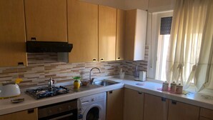 A compact kitchen with a washing machine, a stove, and a sink. - Apartment with TERRACE ON THE SEAwith breathtaking views. 50 meters from the beach (Gela)