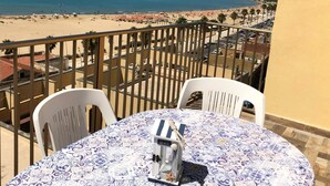 A balcony with a table and chairs, overlooking a beach and ocean. - Apartment with TERRACE ON THE SEAwith breathtaking views. 50 meters from the beach (Gela)