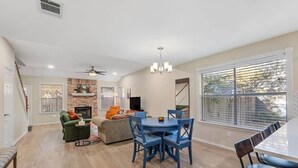 A spacious living area with a fireplace, a dining table with chairs, and a large window with blinds. - Spacious Home + Hot tub + Fire Pit + Play Loft (Cedar Park)