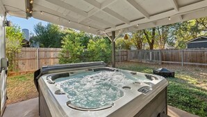 A hot tub under a covered patio with a wooden fence and trees in the background. - Spacious Home + Hot tub + Fire Pit + Play Loft (Cedar Park)