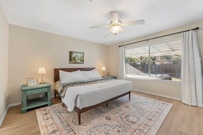 A bedroom with a bed, nightstands, a ceiling fan, a window with curtains, and a view of the outside. - Spacious Home + Hot tub + Fire Pit + Play Loft (Cedar Park)