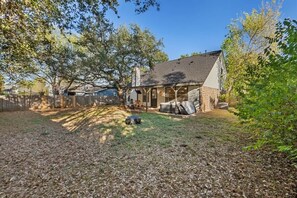 A backyard with a house, a covered patio, and a lawn. - Spacious Home + Hot tub + Fire Pit + Play Loft (Cedar Park)