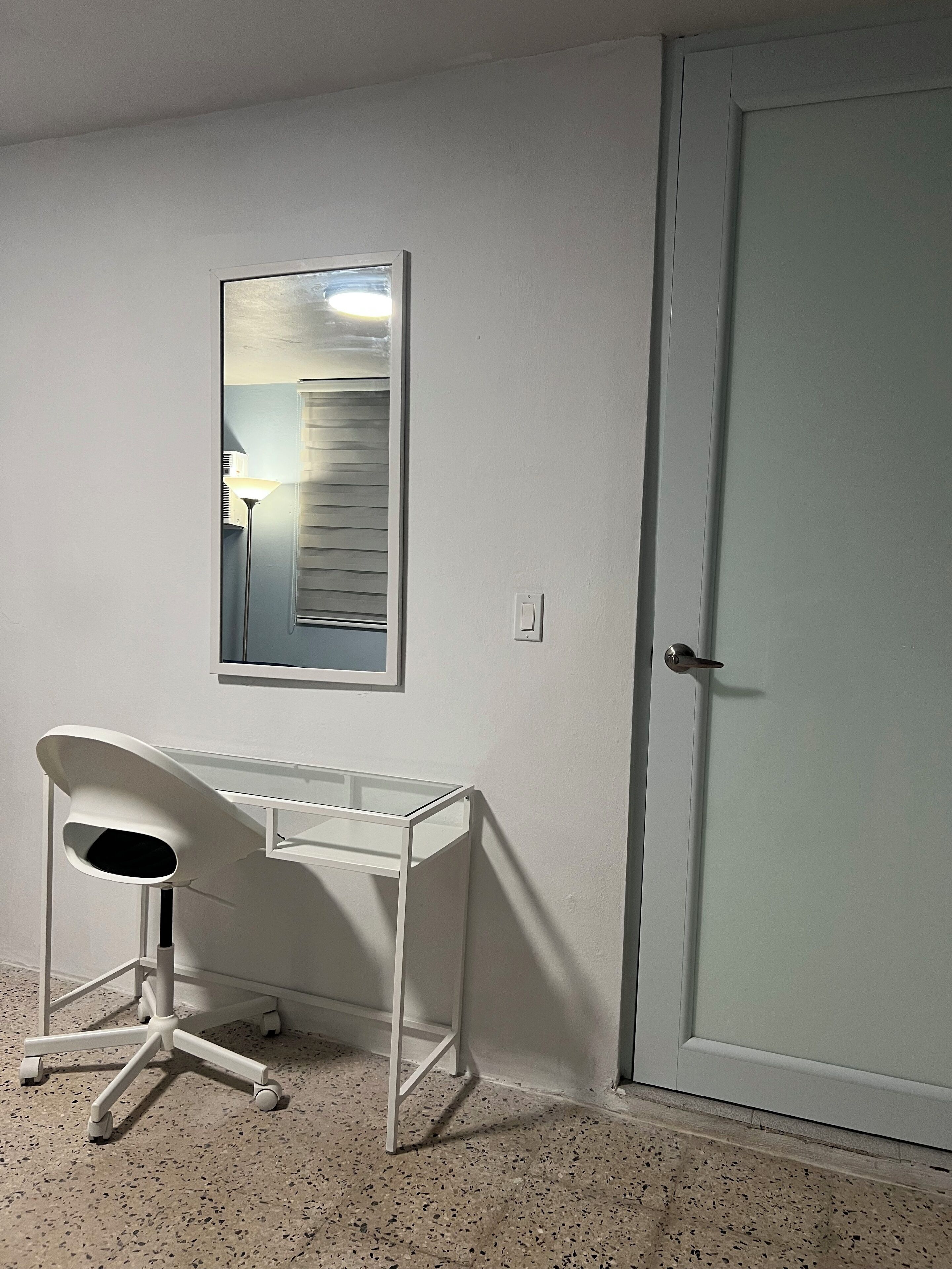A corner room with a white desk, a mirror, and a door.