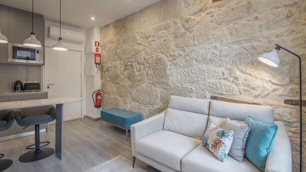 A modern kitchen with a stone wall, a white sofa with cushions, a bar area, and a fire extinguisher. - Ribeira Apartments Baixa (Porto)