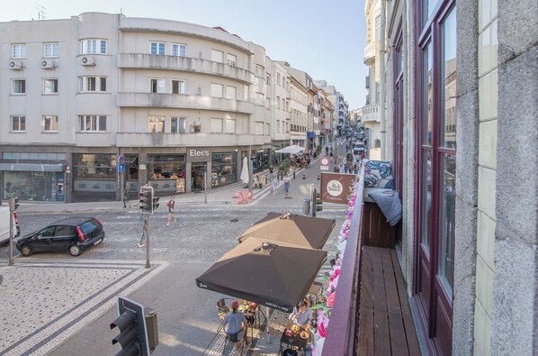 Une vue de rue avec des immeubles, un café doté d’une terrasse, et une voiture garée.