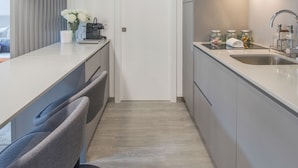 Una cocina moderna con encimera blanca, sillas grises y pileta de acero inoxidable.