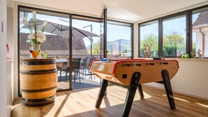 Una habitación con mesa de futbolín, un barril de madera y vistas amplias por las ventanas.