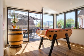 A room with a foosball table, a wooden barrel, and a view through large windows.