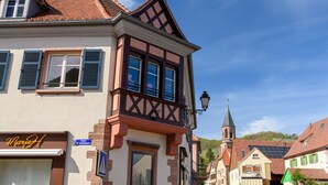 Un edificio tradicional europeo con un tejado a dos aguas, una torre de iglesia visible y un letrero que indica 'Rue de Gonsbach'.
