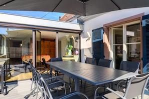 Un espace extérieur abrité, aménagé pour les repas, avec une table et des chaises, un buffet en bois et une porte vitrée donnant sur un espace intérieur.