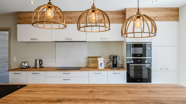 Una cocina moderna con armarios de madera, un refrigerador de acero inoxidable, una cafetera Bosch y tres lámparas colgantes con bombillas expuestas.