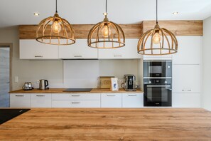 Une cuisine moderne avec des meubles en bois, un réfrigérateur en acier inoxydable, une machine à café Bosch et trois suspensions avec des ampoules apparentes.