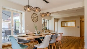 Un comedor con una mesa de madera dispuesta para seis, rodeada de sillas modernas, un espejo grande y un reloj de pared.