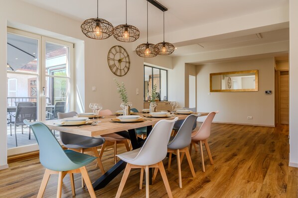 Un coin repas avec une table en bois dressée pour six personnes, entourée de chaises modernes, d’un grand miroir et d’une horloge murale.