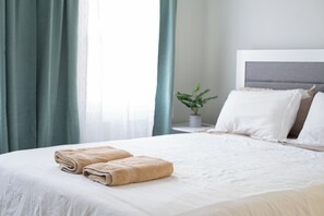 A neatly made bed with two folded towels, a potted plant, and a bedside table with a lamp. - 7 Min to NYC / Modern New Apartment (North Bergen)