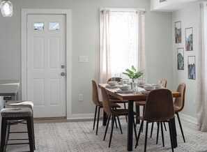 A dining area with a table set for four, surrounded by chairs, a potted plant, and artwork on the walls. - 7 Min to NYC / Modern New Apartment (North Bergen)