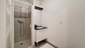 Un bagno con cabina doccia in vetro, un lavandino bianco con piano d'appoggio nero e un armadietto bianco.