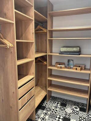 Un armario de madera con varios estantes, cajones y una barra para colgar, además de un suelo de baldosas.