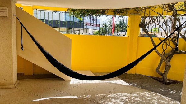 A hammock in a yellow-walled room with a staircase and a tree.