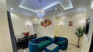 A living room with a sectional sofa, a coffee table, a chandelier, and wall art. - Magnificent residence with luxury concierge service in Brazzaville (Brazzaville)