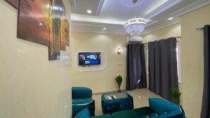 A living room with teal sofas, a chandelier, a flat-screen TV, and a wall-mounted air conditioner. - Magnificent residence with luxury concierge service in Brazzaville (Brazzaville)