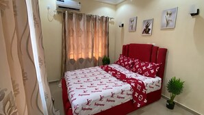 A bedroom with a red bedspread, a potted plant, and artwork on the wall. - Magnificent residence with luxury concierge service in Brazzaville (Brazzaville)