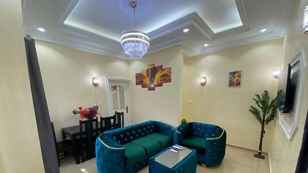 A living room with a sectional sofa, a coffee table, a chandelier, and wall art. - Magnificent residence with luxury concierge service in Brazzaville (Brazzaville)