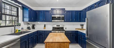 Een moderne keuken met blauwe kastjes, roestvrijstalen apparatuur en een houten eiland.