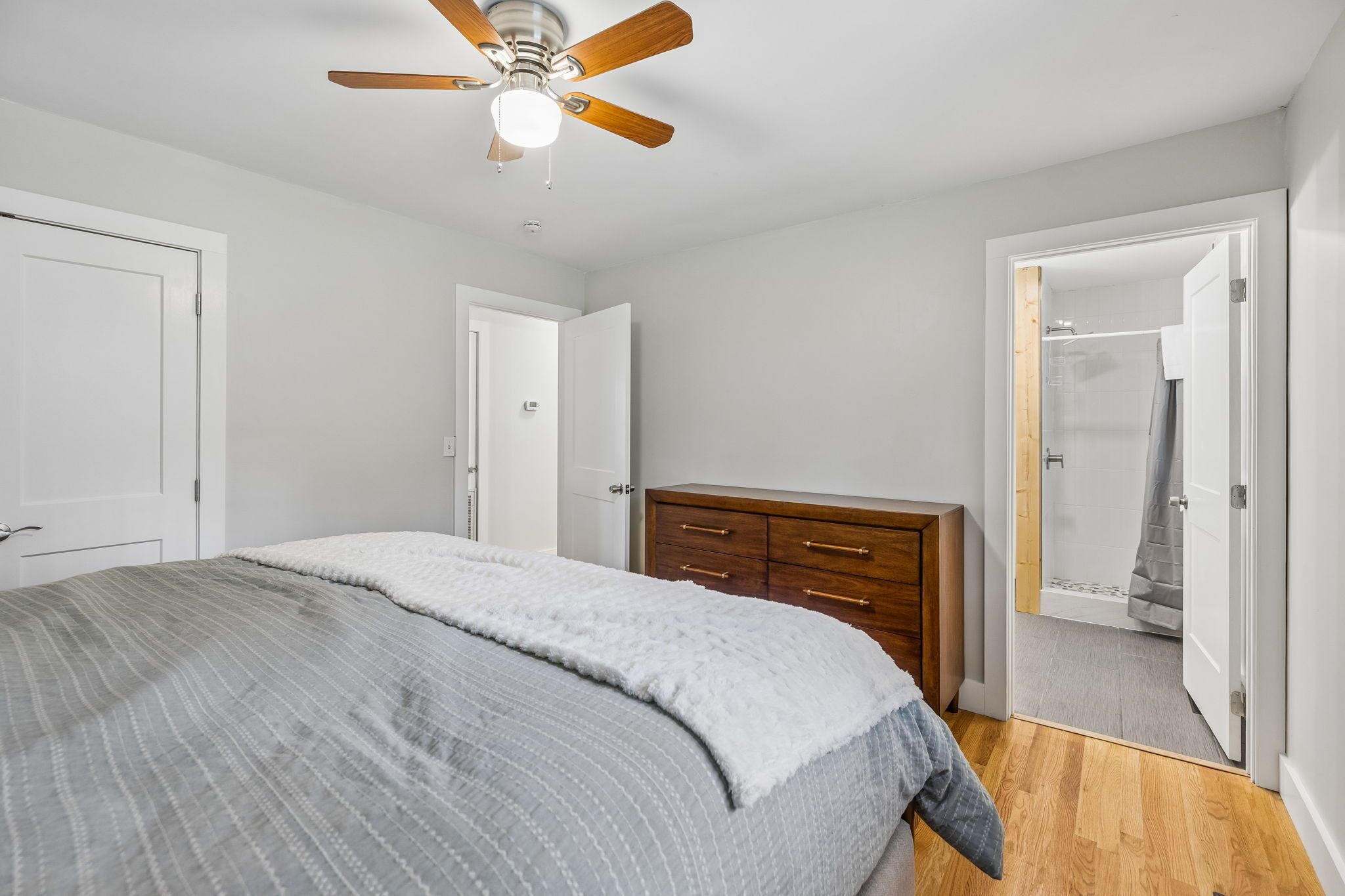 Une chambre à coucher avec un lit, une commode en bois, un ventilateur de plafond et une porte de douche.