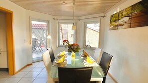 A dining area with a glass table, chairs, a vase with flowers, and a painting on the wall.