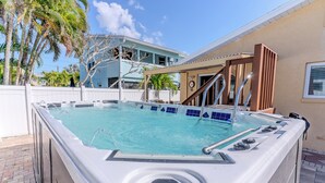 Un jacuzzi con un deck de baldosas, una pérgola de madera y una piscina al fondo.
