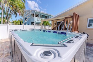 Ein Whirlpool mit einer gefliesten Terrasse, einer Holzhütte und einem Pool im Hintergrund.