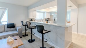 Una cocina moderna con encimera de mármol, dos taburetes de bar, un sofá gris y una mesa de centro de madera.