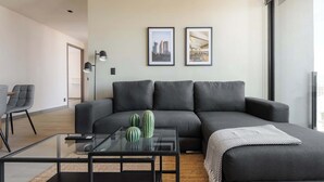 Een moderne woonkamer met een grijze bank, een glazen salontafel en twee ingelijste foto’s aan de muur.