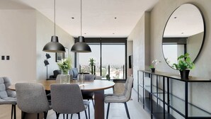 Een moderne eetruimte met een ronde tafel, grijze stoelen, hanglampen en een groot raam met uitzicht op de stad.