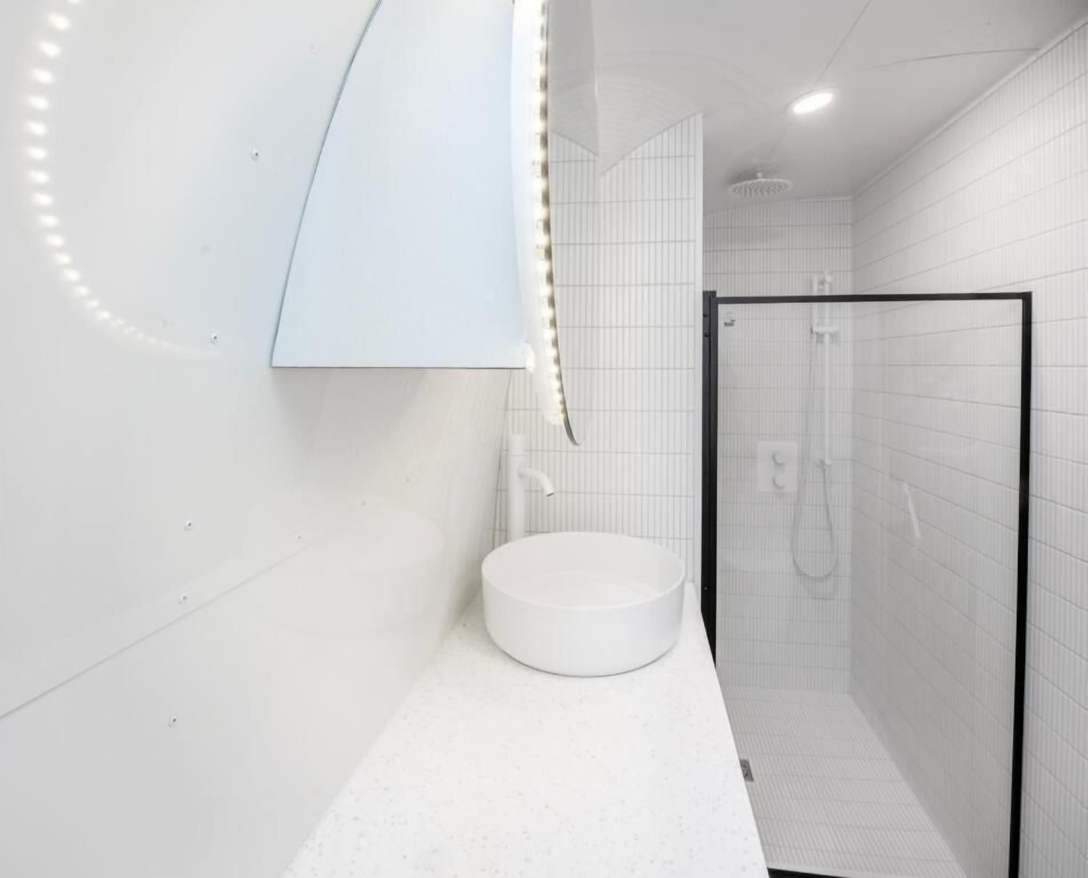 Ein modernes Badezimmer mit einem runden Waschbecken, einer Duschkabine aus Glas und einem wandmontierten Spiegel.