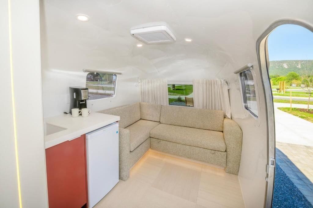 A compact kitchen with a refrigerator, a coffee maker, and a window with curtains.