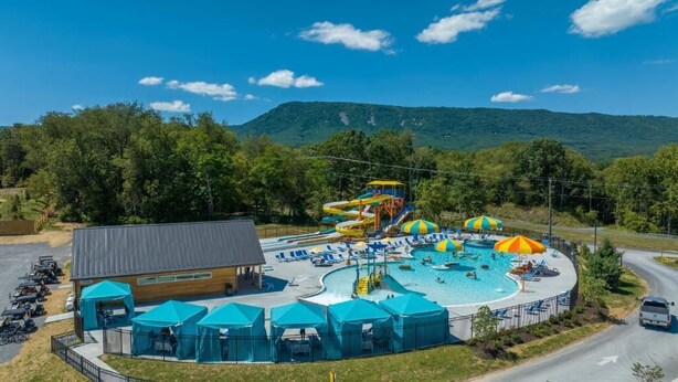 A water park with multiple slides and a swimming pool, surrounded by trees and a mountain in the background. - Luray RV Resort on Shenandoah River (Luray)