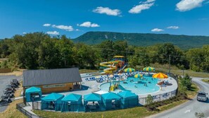 A water park with multiple slides and a swimming pool, surrounded by trees and a mountain in the background. - Luray RV Resort on Shenandoah River (Luray)