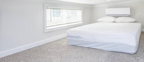 A bedroom with a bed, a window with blinds, and a white ceiling.