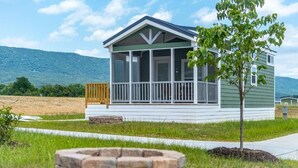 A single-story house with a porch, a small tree in front, and a stone fire pit. - Luray RV Resort on Shenandoah River (Luray)