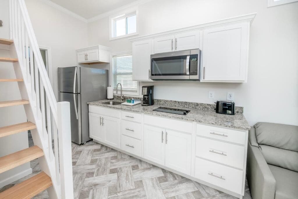 A modern kitchen with white cabinets, stainless steel appliances, and a herringbone-patterned floor.