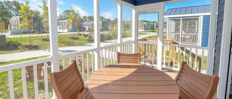 A covered outdoor patio with a round table and four wooden chairs, overlooking a residential area.