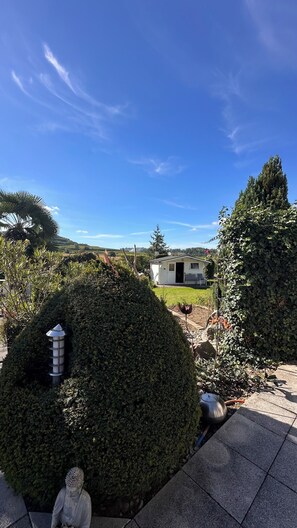 Ein gepflegter Garten mit einer Statue, einer kleinen Gartenhütte und blauem Himmel.