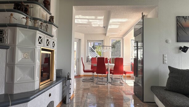 Una cocina moderna con muebles blancos, una zona de comedor con sillas rojas y una sala de estar con sofá gris.