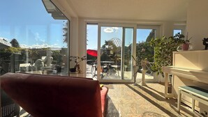 Una habitación con un sofá rojo, una mesa de vidrio y vistas a un patio exterior con una mesa y sillas.